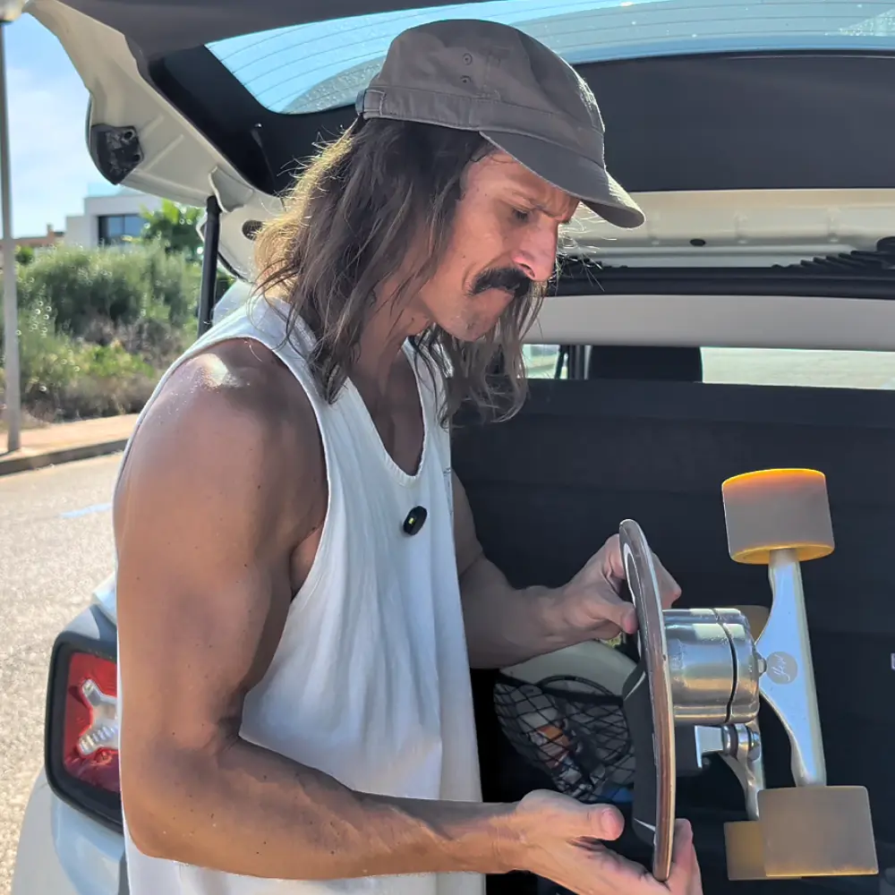 Eitiboy revisa su surfskate junto al maletero abierto del coche.